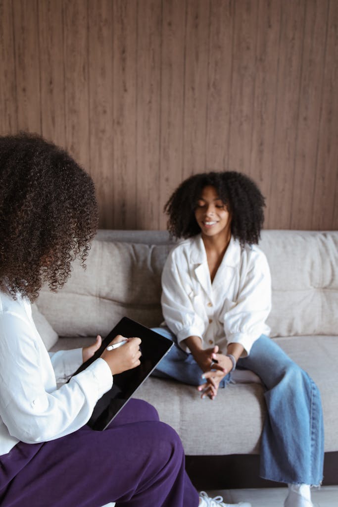 Two women discussing therapy while using a tablet in a cozy room.